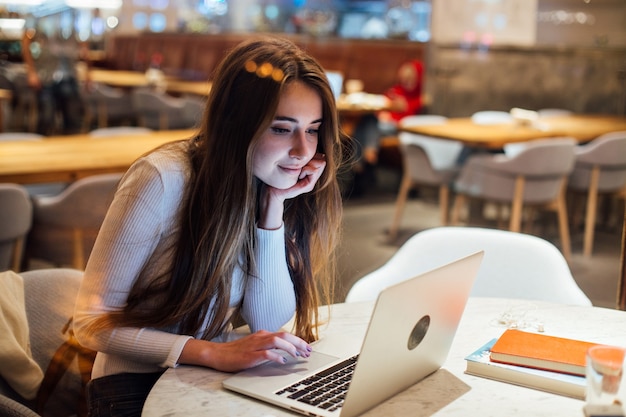 Linda chica trabaja en la computadora portátil en la cafetería hipster