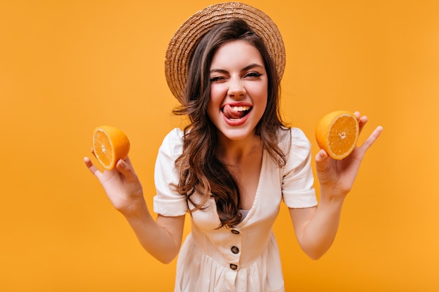 Foto gratuita linda chica en traje blanco y canotier lamió, guiña un ojo y sostiene naranjas.