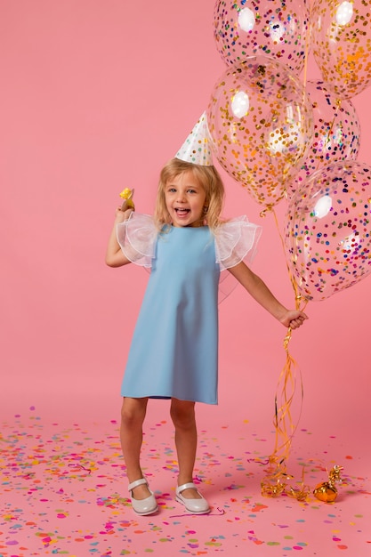 Linda chica en traje con globos y gorro de fiesta