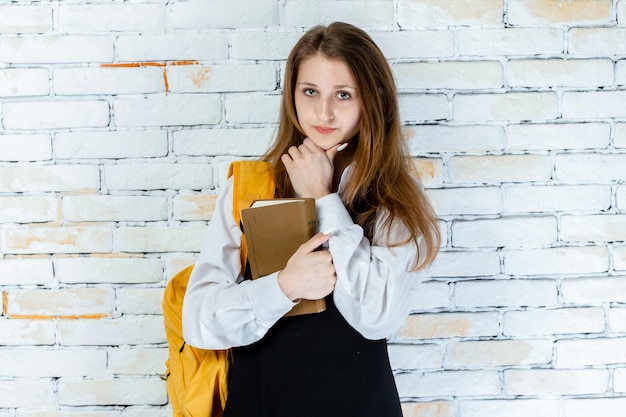 Linda chica en uniforme escolar sosteniendo su libro y parece pensativa