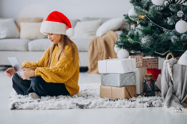 Linda chica usando computadora por árbol de Navidad