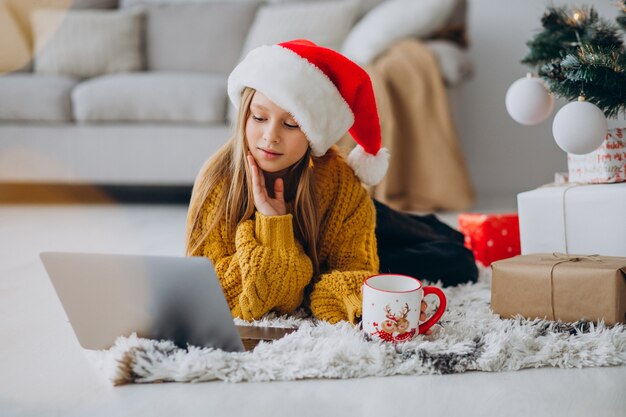 Linda chica usando computadora por árbol de Navidad