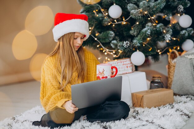 Linda chica usando computadora por árbol de Navidad