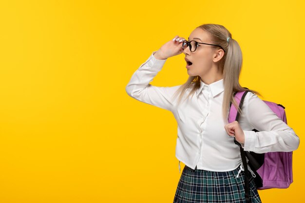 Linda colegiala del día mundial del libro mirando lejos en gafas con mochila rosa