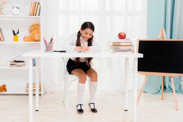 Linda colegiala sentada en el escritorio y haciendo ejercicio en el aula