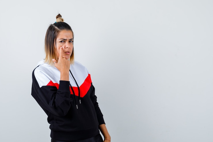 Foto gratuito linda dama apuntando a su párpado en sudadera con capucha y mirando triste, vista frontal.