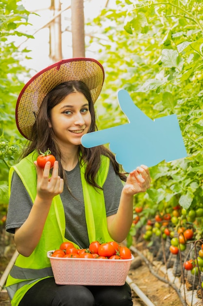Linda dama sosteniendo tomate y tablero de ideas en el invernadero