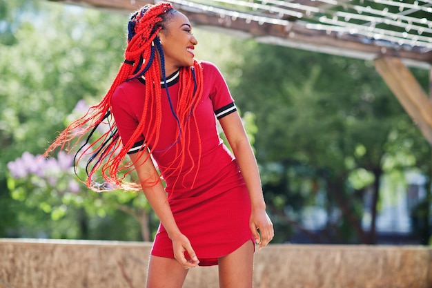 Foto gratuita linda y delgada chica afroamericana en vestido rojo con rastas en movimiento divirtiéndose en la calle elegante modelo negro