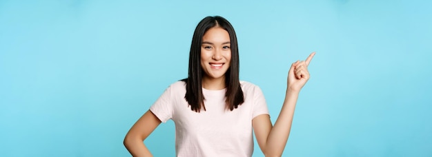 Linda estudiante morena asiática sonriente apuntando a la esquina superior izquierda que muestra el banner promocional del nombre de la empresa