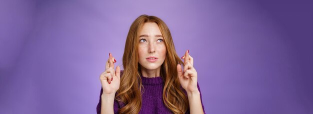 Linda estudiante pelirroja preocupada con pecas entrecerrando los ojos y concentrándose en pedir un deseo como cruce