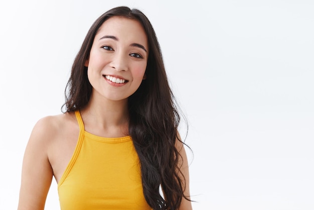 Foto gratuita linda y gentil tímida joven novia asiática con cabello largo y oscuro sonriendo tiernamente con cuidado y amor inclinando la cabeza de pie fondo blanco feliz y alegre con un aspecto encantador copiar espacio