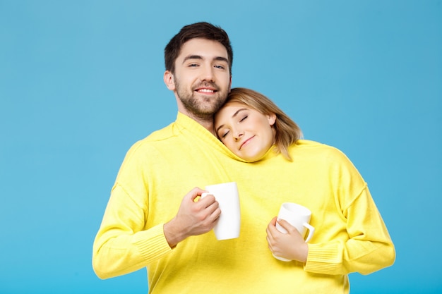 Linda hermosa pareja sonriendo sosteniendo copas sobre pared azul