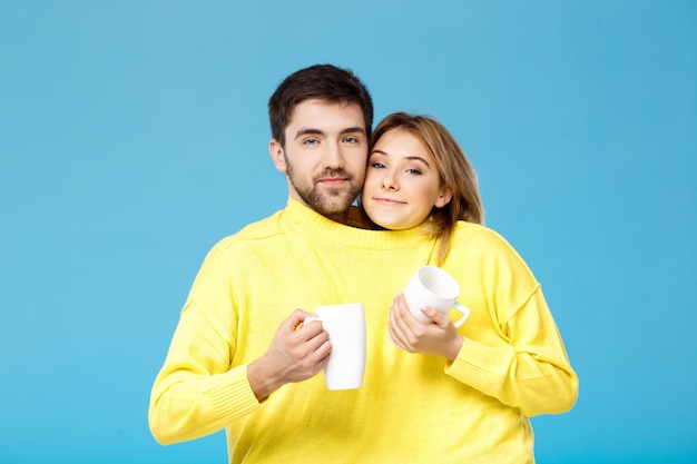 Linda hermosa pareja sonriendo sosteniendo copas sobre pared azul