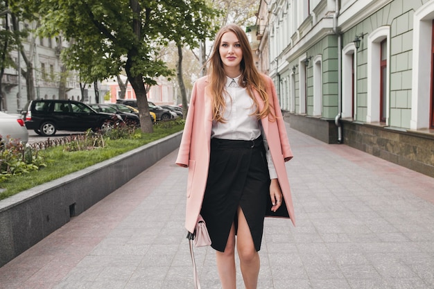 Linda joven y elegante hermosa mujer caminando en la calle, vestida con abrigo rosa, bolso, camisa blanca, falda negra, traje de moda, tendencia de otoño, sonriendo feliz, accesorios