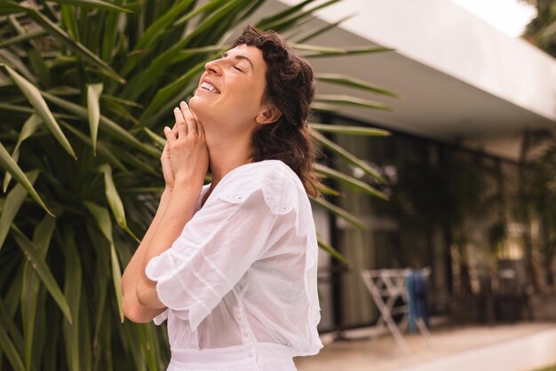 Linda joven morena caucásica con vestido blanco cerrando los ojos disfruta de la naturaleza relajándose al aire libre