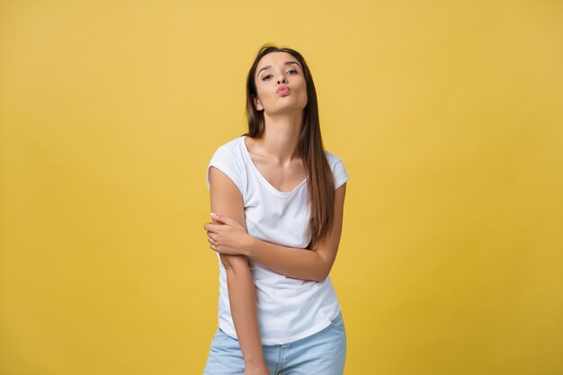 Linda joven mujer feliz soñando en camiseta blanca aislada sobre fondo amarillo dando airkiss