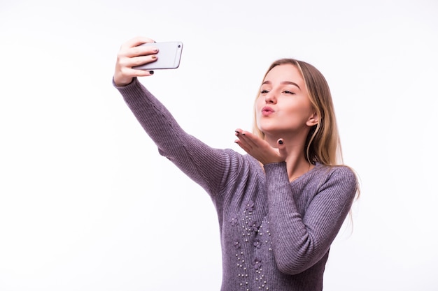 Linda joven mujer feliz soñando en camiseta a rayas aislada en la pared blanca tomando un selfie y dando beso de aire