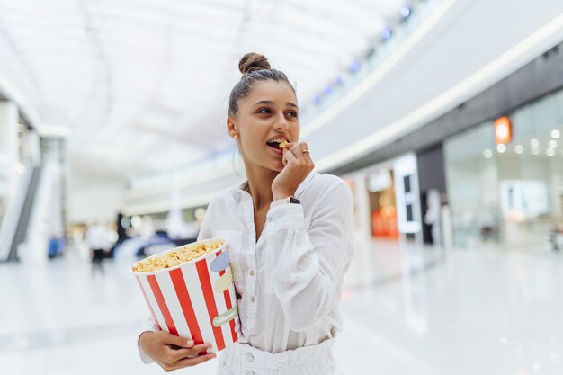 Linda joven mujer sosteniendo palomitas de maíz en el fondo del centro comercial