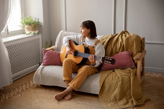 Foto gratuita linda joven tocando la guitarra en el interior