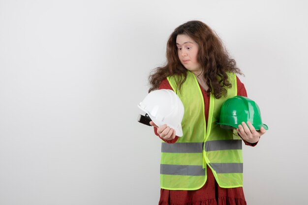 Linda jovencita con síndrome de down de pie en chaleco y sosteniendo cascos protectores.