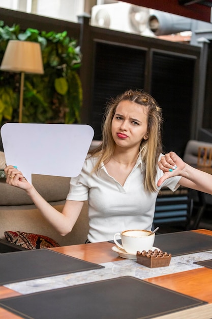 Linda jovencita sosteniendo un tablero de ideas y un gesto con el pulgar hacia abajo