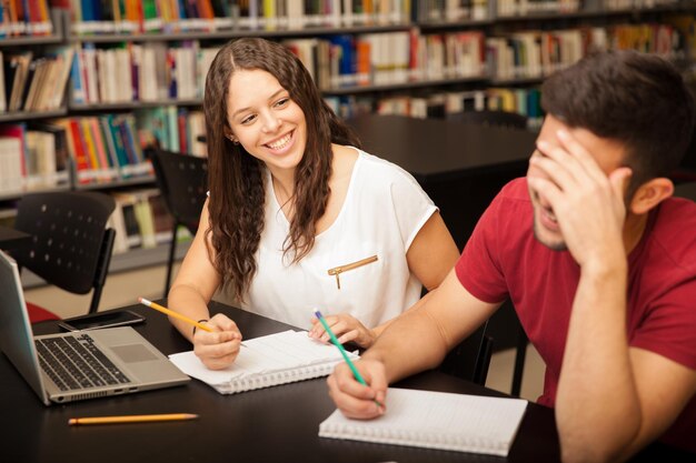 Linda morena coqueteando y riendo con un amigo que le gusta mientras estudia en la biblioteca