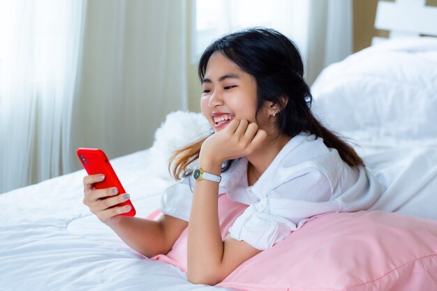 Linda mujer adolescente alegre con teléfono inteligente en la cama