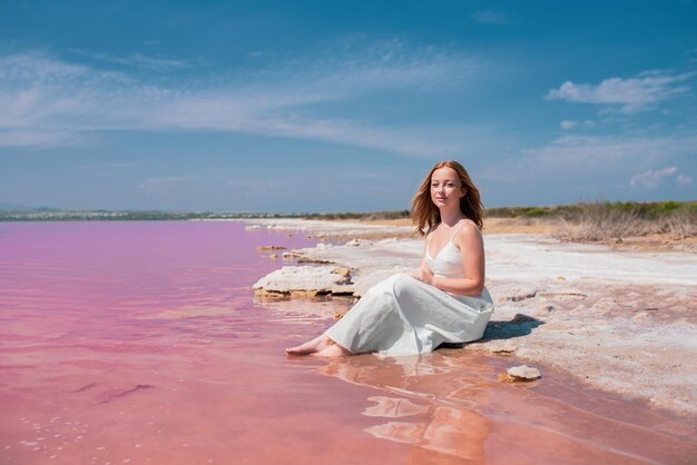 Linda mujer adolescente con vestido blanco sentada en un increíble lago rosa