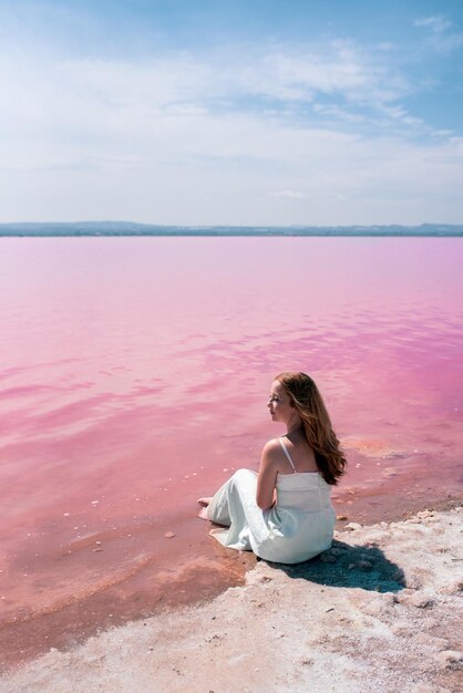 Linda mujer adolescente con vestido blanco sentada en un increíble lago rosa