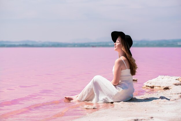 Linda mujer adolescente con vestido blanco sentada en un increíble lago rosa