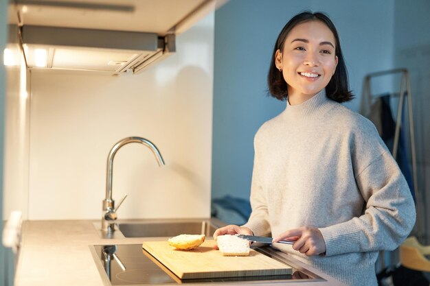 Linda mujer asiática haciéndose tostadas cortar pan preparando sándwich en la cocina