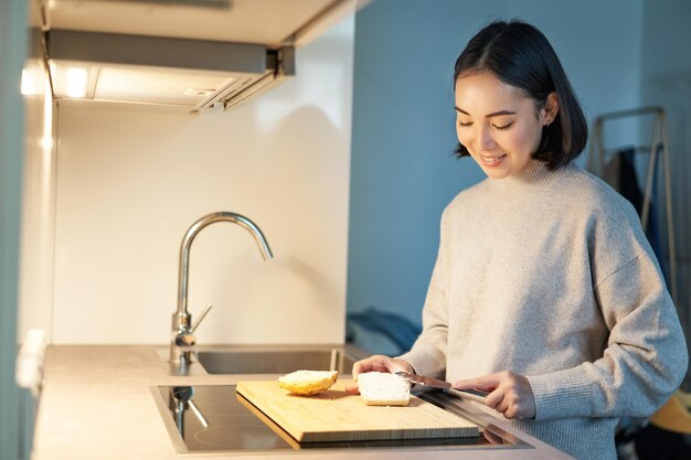 Linda mujer asiática haciéndose tostadas cortar pan preparando sándwich en la cocina