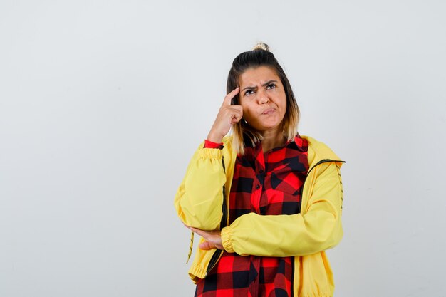 Linda mujer en camisa, chaqueta sosteniendo el dedo en las sienes, mirando hacia arriba y mirando pensativo, vista frontal.