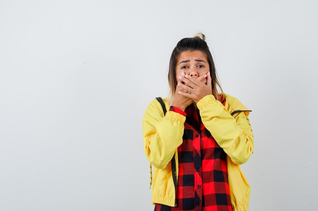 Linda mujer cogidos de la mano en la boca en camisa, chaqueta y mirando ansiosa. vista frontal.