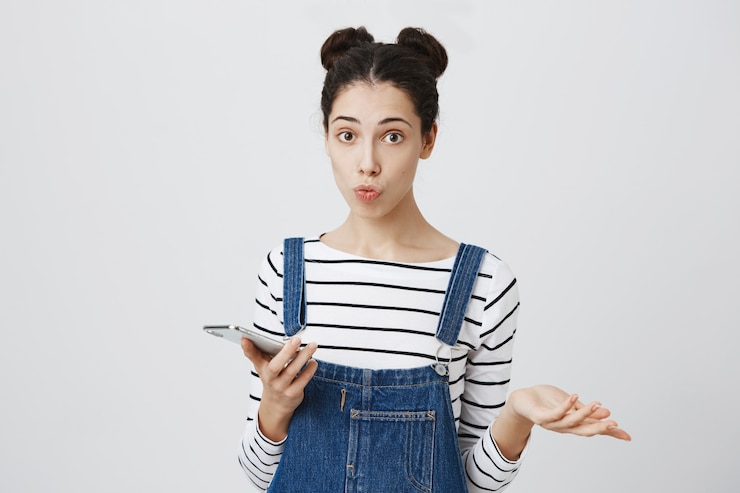 Foto gratuito linda mujer confundida encogiéndose de hombros como usando teléfono móvil