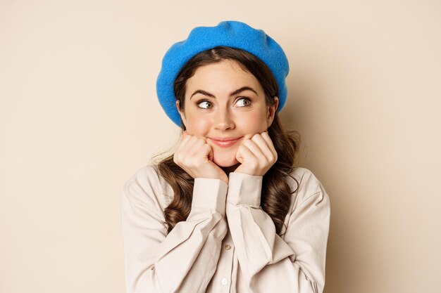 Linda mujer coqueta posando, sonriendo y mirando a un lado con pensamiento, cara de ensueño, algo de imagen, de pie sobre fondo beige