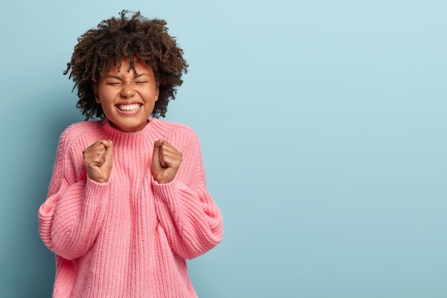 Linda mujer emotiva feliz de lograr la meta y lograr un buen resultado, aprieta los puños, sonríe feliz