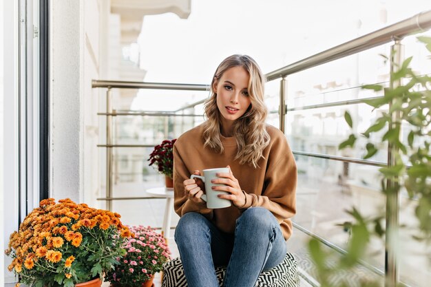 Linda mujer europea bebiendo té en la terraza. retrato de una chica rubia interesada disfrutando de un café.