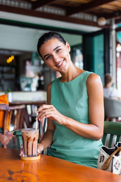 Linda mujer feliz tranquila elegante en vestido verde de verano se sienta con café en la cafetería disfrutando de la mañana