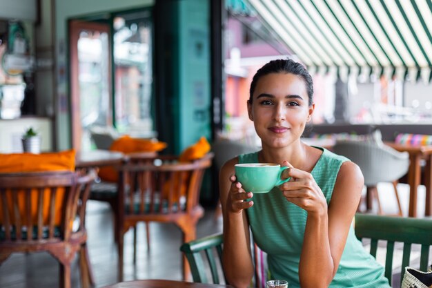 Linda mujer feliz tranquila elegante en vestido verde de verano se sienta con café en la cafetería disfrutando de la mañana