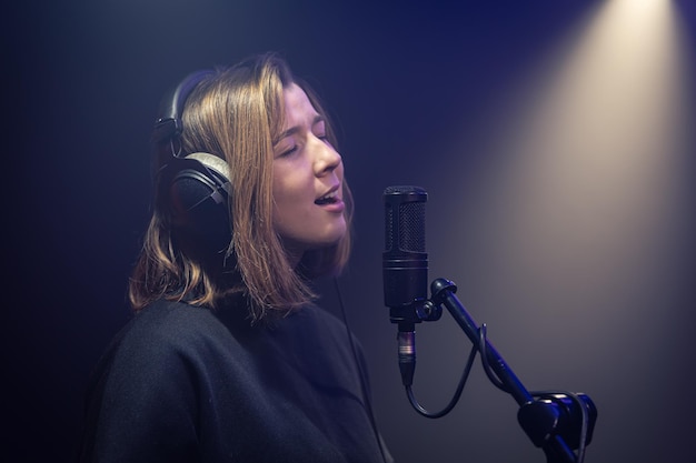 Foto gratuita una linda mujer joven en auriculares canta en un micrófono en una habitación oscura