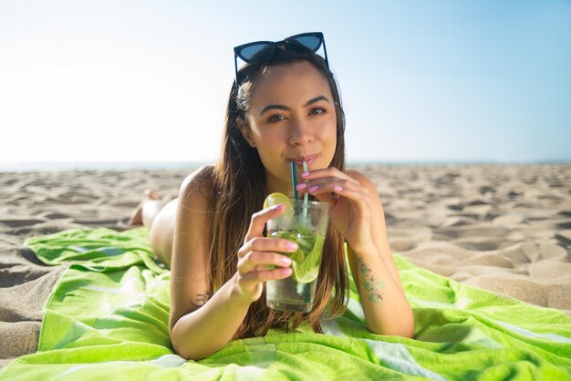 Linda mujer joven bebiendo un cóctel. Mujer sosteniendo vaso con bebida fría brillante