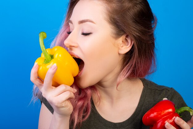 Linda mujer joven con cabello rosado mordiendo un pimiento amarillo