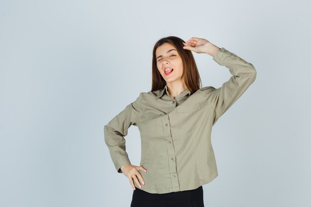 Linda mujer joven mostrando gesto de saludo mientras guiña un ojo en camisa y parece confiado. vista frontal.