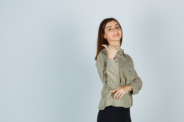 Linda mujer joven mostrando el pulgar hacia arriba en camisa, falda y mirando feliz. vista frontal.