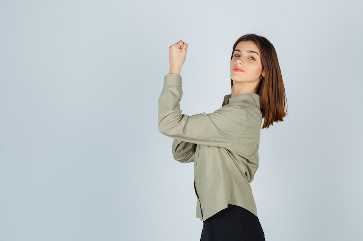 Foto gratuito linda mujer joven que muestra los músculos del brazo en camisa, falda y parece confiada.