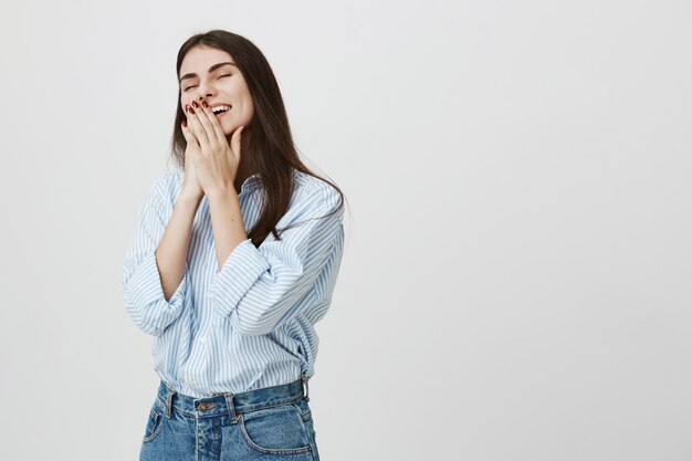 Linda mujer joven ríe, tapa sonrisa con las manos