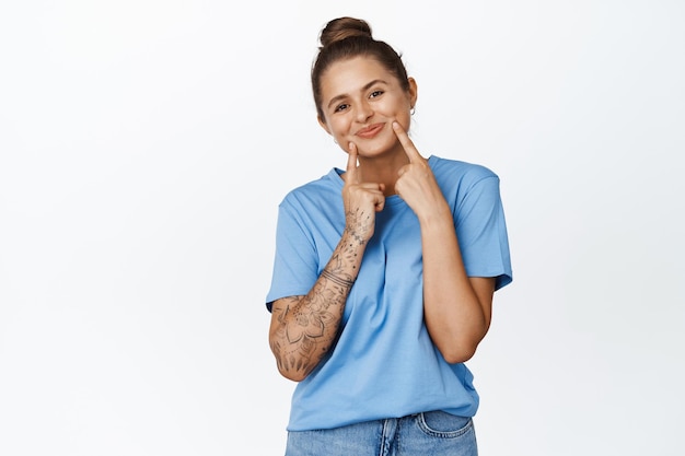 Foto gratuita linda mujer joven sonriendo, mostrando sus hoyuelos en las mejillas, de pie encantadora en camiseta azul sobre fondo blanco.