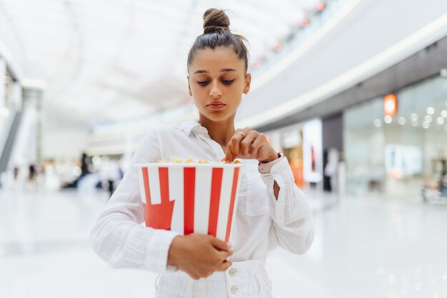 Linda mujer joven sosteniendo palomitas de maíz en el centro comercial