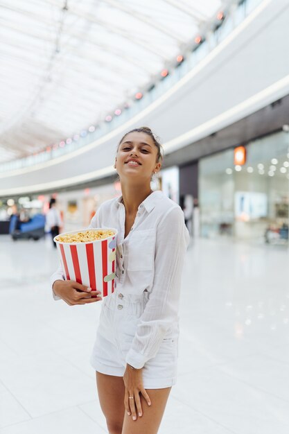 Linda mujer joven sosteniendo palomitas de maíz en el fondo del centro comercial